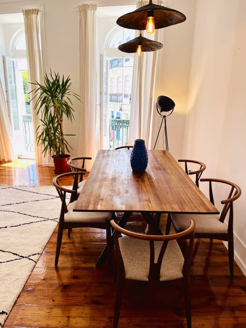 Modern dining area in Lisbon apartment with wooden table, mid-century chairs, pendant lights, and garden view through tall
