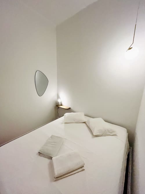 Minimalist bedroom in Royal Prince Garden Apartments, Lisboa, with white bed, pillows, towels, and oval mirror on cream walls