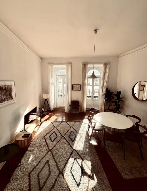 Bright apartment living room with dining table, balcony doors, geometric rug, and city views in Lisboa