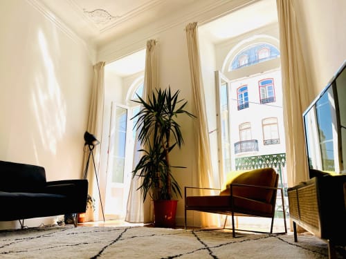 Bright Lisbon apartment living room with modern furniture, tall windows overlooking city, indoor plants, and natural light