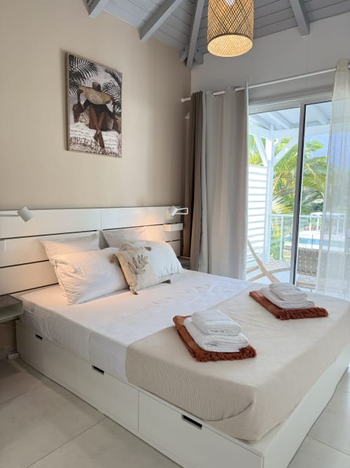 Chambre moderne à Domaine de la Glacière, Petit Bourg avec lit blanc, portes donnant sur l'océan et décoration tropicale