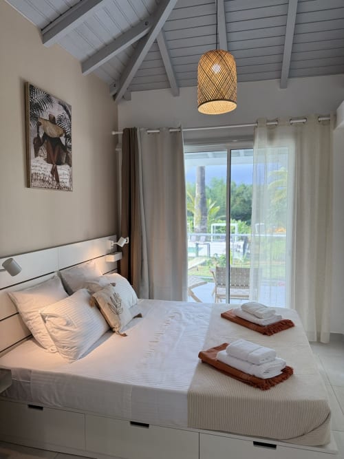 Chambre moderne à la Domaine de la Glacière avec lit blanc, suspension tissée et vue sur l'océan par portes vitrées à Petit Bourg