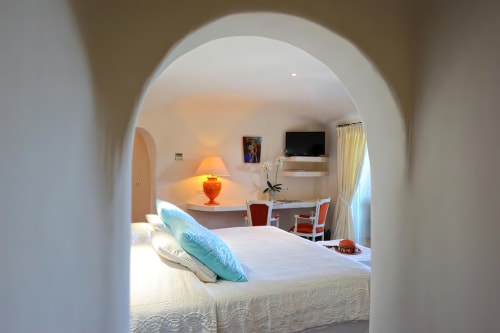 suite lumineuse à l'hôtel Marina Di Cavu à Bonifacio avec porte en arche, lit blanc, coussins turquoise, lampe, bureau et TV 