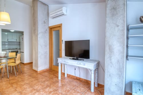 Sala de estar del hotel Finques Garcia Enrich en Palafrugell con TV, consola blanca, cocina americana y suelo de barro cocido