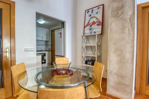 Comedor con mesa redonda de cristal y sillas de madera en Finques Garcia Enrich, Palafrugell, cocina visible al fondo
