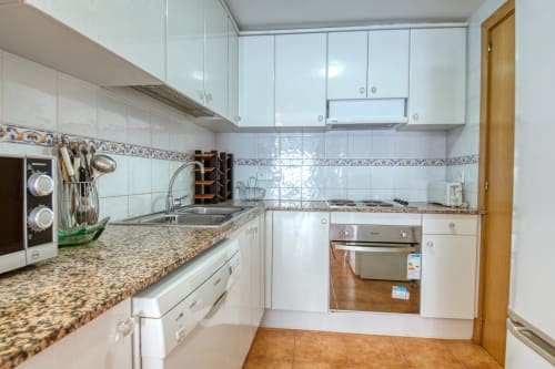Cocina blanca moderna con encimeras de granito, horno de acero inoxidable y salpicadero de azulejos azules en Finques Garcia Enrich
