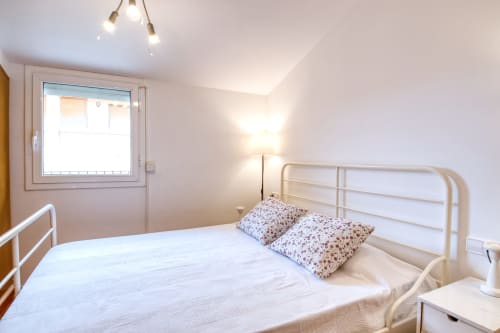 Dormitorio luminoso en Finques Garcia Enrich de Palafrugell con cama de metal blanco y almohadas florales