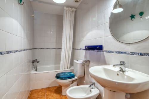 Baño limpio con azulejos blancos, doble lavabo, inodoro, bañera y ducha en el hotel Finques Garcia Enrich en Palafrugell