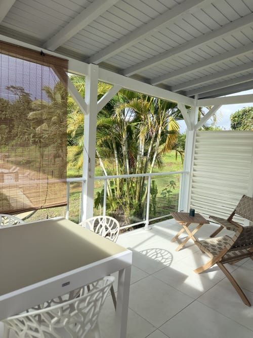 Bungalow Ixora à la Domaine de la Glacière avec terrasse couverte, vue sur piscine, chaises blanches et jardin tropical avec palmiers