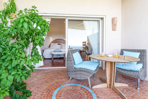 Espace de détente en terrasse de la Villa Marina Di Cavu à Bonifacio avec chaises en rotin, table en bois et vue sur mer par les portes ouvertes