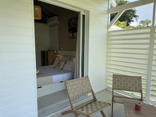 Chambre du bungalow Tiaré au Domaine de la Glacière, Petit-Bourg, avec lit et sièges en terrasse sous volets ajourés