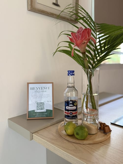 Aménités de bienvenue au Domaine de la Glacière avec rhum, fleur tropicale, citrons verts et pancarte d'accueil au Bungalow Balisier