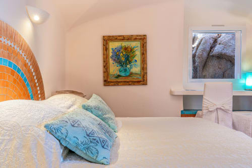 Chambre lumineuse à la Villa Marina Di Cavu à Bonifacio avec coussins bleus à motifs, œuvre florale et vue jardin