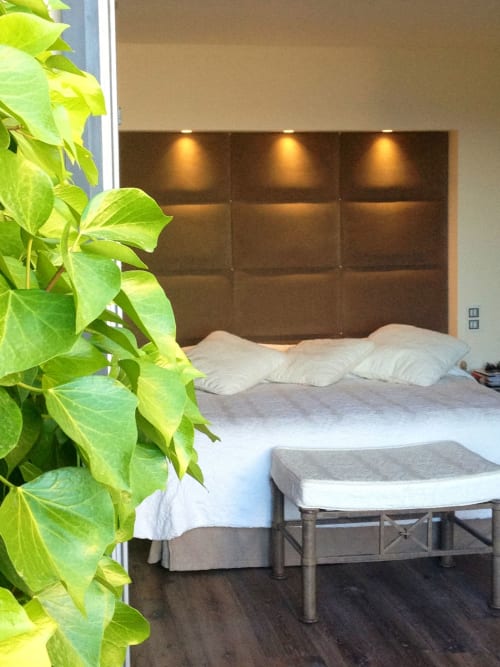 Chambre moderne à la Villa Marina Di Cavu à Bonifacio avec tête de lit capitonnée marron, oreillers blancs, banc, plante verte et décoration sombre
