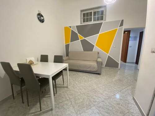 Appartamento Newhouse a Bari con tavolo da pranzo, sedie verdi, divano beige e murale geometrico a parete