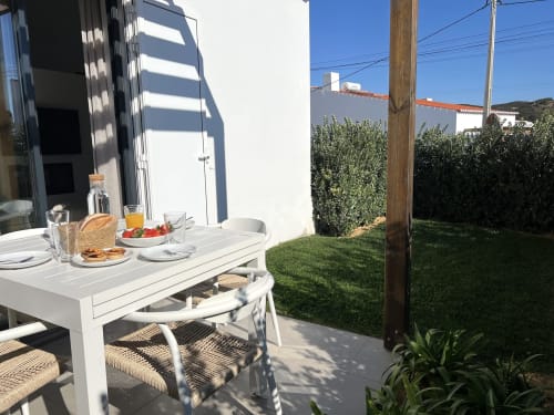 Área de jantar ao ar livre na villa Casa Amado em Bordeira com mesa branca, cadeiras de vime, vista para o jardim e vista para o mar