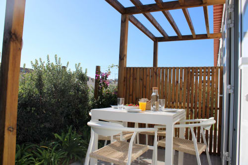 Varanda da villa Casa Amado em Bordeira com mesa de jantar branca, pérgola de madeira, vistas para o jardim e vista do mar.
