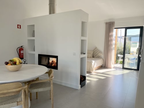 Vila Casa Amado em Bordeira com sala aberta, lareira, área de refeições, vista para o mar através de portas de vidro e quarto