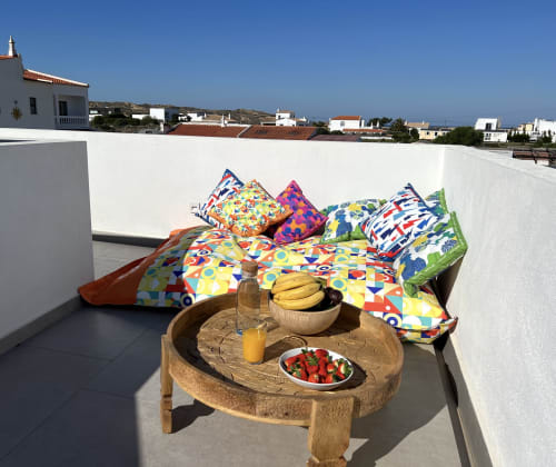 Espaço de estar colorido com almofadas, mesa de madeira com frutas frescas e sucos na villa Casa Amado, Bordeira Portugal
