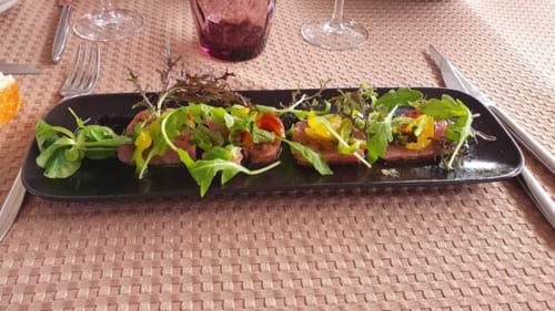 Élégante mise en assiette au Domaine du haut de la Dombes avec jeunes pousses, légumes colorés et vin rouge