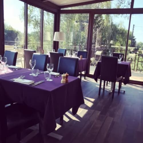 Élégante salle à manger du Domaine du haut de la Dombes avec tables drapées de pourpre, chaises bleues et baies vitrées panoramiques