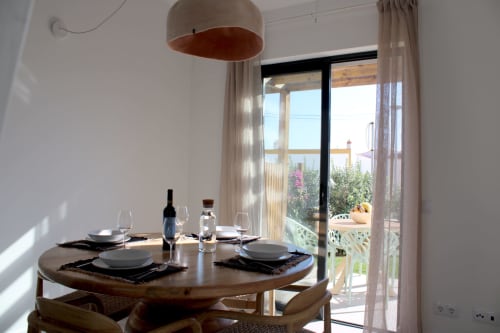 Sala de jantar moderna da vila Casa Amoreira em Bordeira com vista para o mar através de portas de vidro, mesa redonda em madeira, luminária pendente