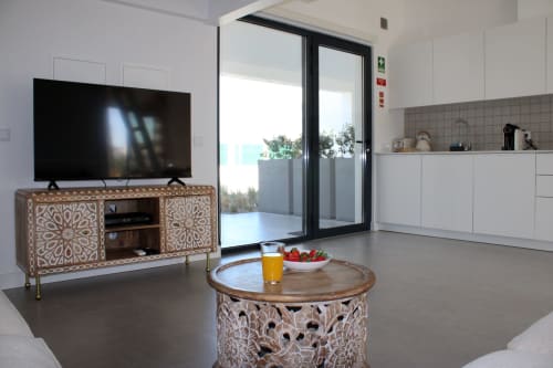 Sala de estar moderna na villa Casa Amoreira, Bordeira, com móveis em madeira entalhada, TV de tela plana e vista para o mar através de vidro