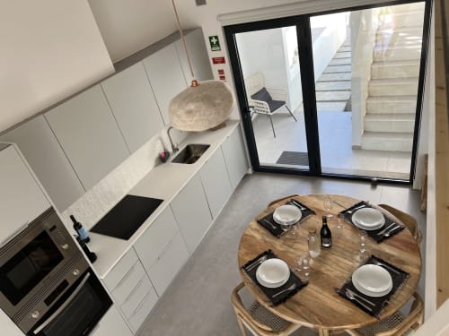 Cozinha moderna branca com sala de jantar na villa Casa Arrifana em Bordeira, Portugal, com mesa de madeira posta para quatro pessoas