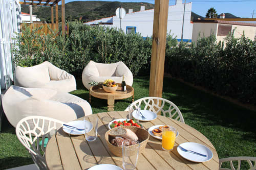 Casa Arrifana villa garden dining area with set table, bean bag chairs, and mountain views in Bordeira, Portugal