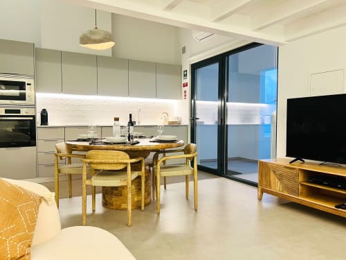 Cozinha e sala de jantar integradas modernas na moradia Casa Arrifana em Bordeira, com móveis em madeira e portas com vista para o mar