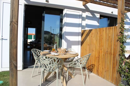 Zona de refeições exterior da villa Casa Castelejo em Bordeira com mesa de madeira, cadeiras brancas e vistas para o mar através de portas de vidro