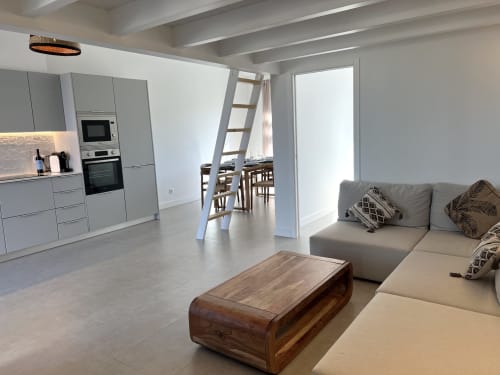 Sala de estar moderna com cozinha, sofá cinzento, mesa de madeira e vista para o mar em Casa Castelejo, Bordeira.