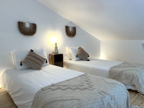 Quarto luminoso com duas camas de solteiro, almofadas listradas, decoração em madeira trançada, luminária e piso de madeira na villa Casa Castelejo