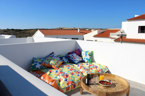 Roupa de cama colorida no terraço da cobertura da villa Casa Castelejo, Bordeira Portugal, com edifícios caiados e vista para o campo