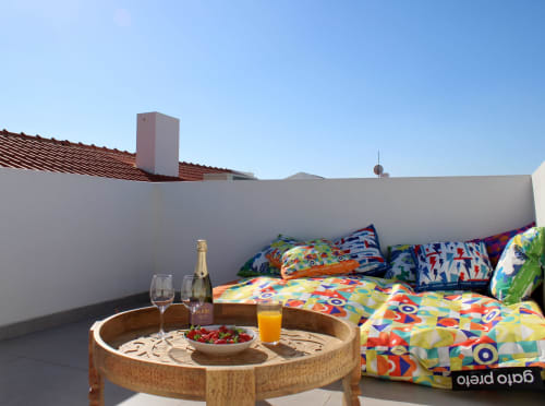 Terraço na cobertura da villa Casa Castelejo em Bordeira com roupa de cama colorida, mesa de madeira, champanhe e vistas para o mar.