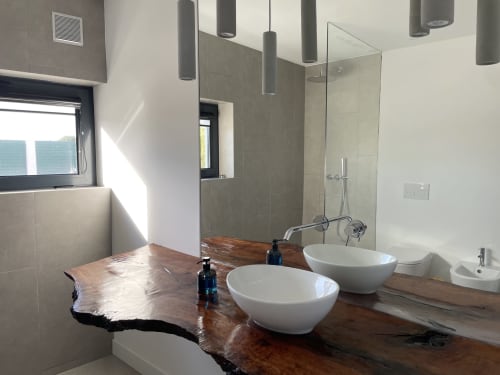 Banheiro moderno da villa Casa Castelejo em Bordeira com duas pias de porcelana, bancada em madeira e box de vidro.