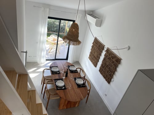 Sala de jantar moderna da villa Casa Cordoama em Bordeira com mesa de madeira, luminárias pendentes trançadas e vista para o mar através de vidro