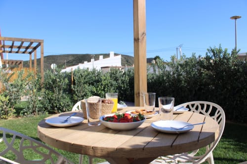 Mesa de jantar ao ar livre na villa Casa Cordoama em Bordeira com frutas frescas, bebidas e pratos brancos com vista para o jardim