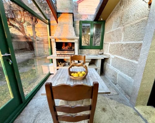 Comedor al aire libre con muros de piedra, sillas de madera, chimenea y vistas al mar en villa Vila Arume en Baiona