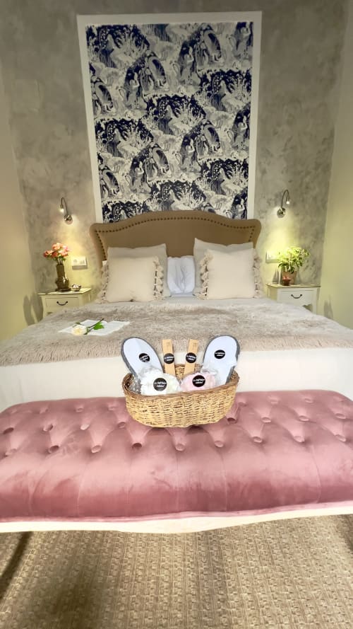 Elegante dormitorio en apartamento de Puerto Santa María con cabecera tostada, almohadas blancas, arte azul toile, rosa