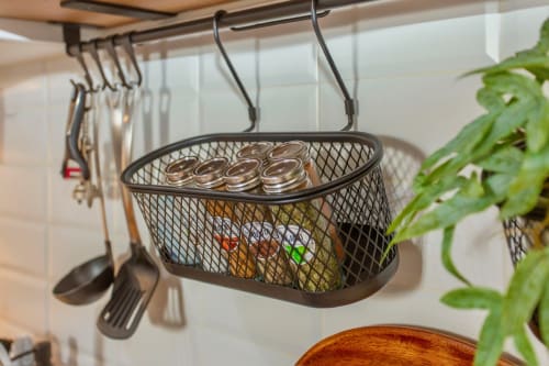 Cesta colgante de malla negra con frascos y utensilios de cocina en apartamento de Puerto Santa María