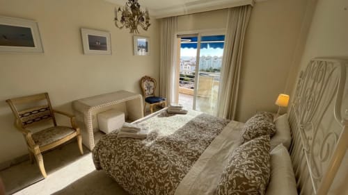 Spacious bedroom with twin beds, sea view balcony, and Puerto Banús coastline visible through glass doors at Marbella Home