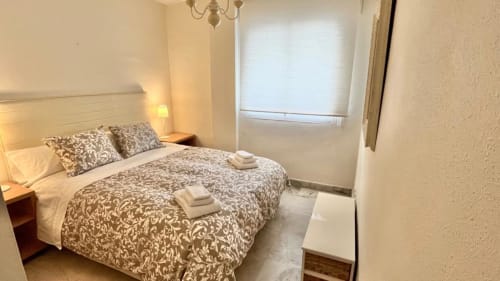Modern bedroom in Marbella Home Rentals Marina Banús apartment with patterned bedding, side tables, and window with sea view