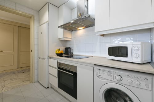 Modern kitchen in Marina Banús apartment with white cabinets, stainless steel appliances, washing machine, and microwave at