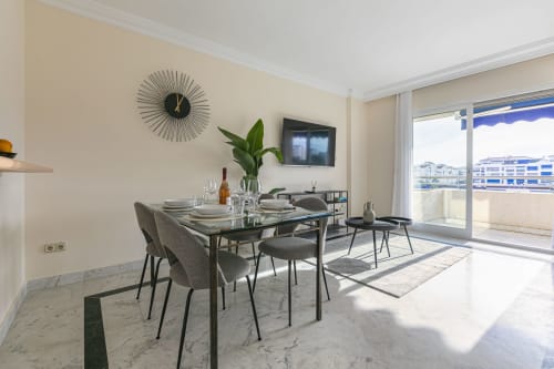 Modern dining area in Marbella apartment with sea view, marble floors, contemporary furniture, and balcony overlooking Puerto