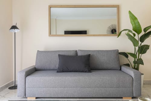 Modern gray sofa bed in Marbella apartment with plant, mirror, and floor lamp in bright living room