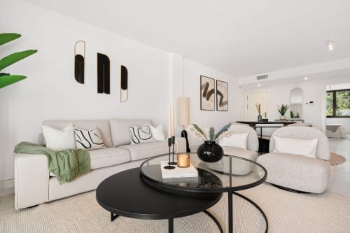 Modern living room in Marbella luxury apartment with beige sofa, accent chairs, and black coffee tables
