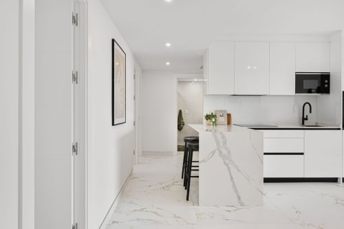 Modern white kitchen with marble island, black accents, and stainless steel appliances in Marbella apartment