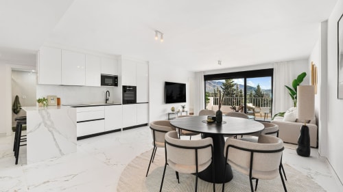 Modern luxury apartment kitchen and dining area in Marbella with mountain views, white cabinetry, black round table, and