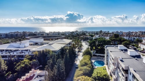 Aerial view of Marbella apartment with pool, Mediterranean Sea, white buildings, green landscape, and coastal town